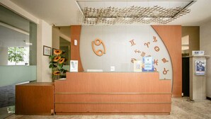 Ein moderner Empfangstresen mit Holzoptik und Glastrennwand. An der Wand befinden sich Bilder in Rahmen und eine Vase mit Sonnenblumen.