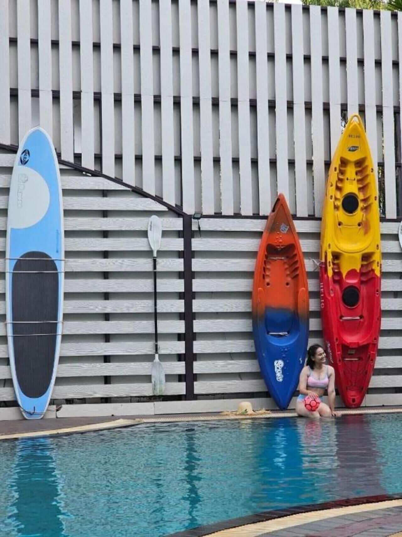 Een zwembad met kayaks en een paddleboard, leunend tegen een witte omheining.