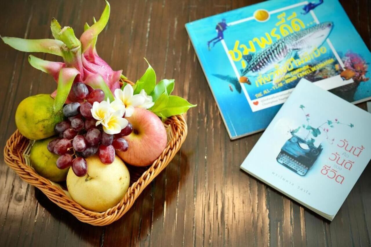A wicker basket with fruits and flowers, a book with a blue cover, and another book with a white cover.