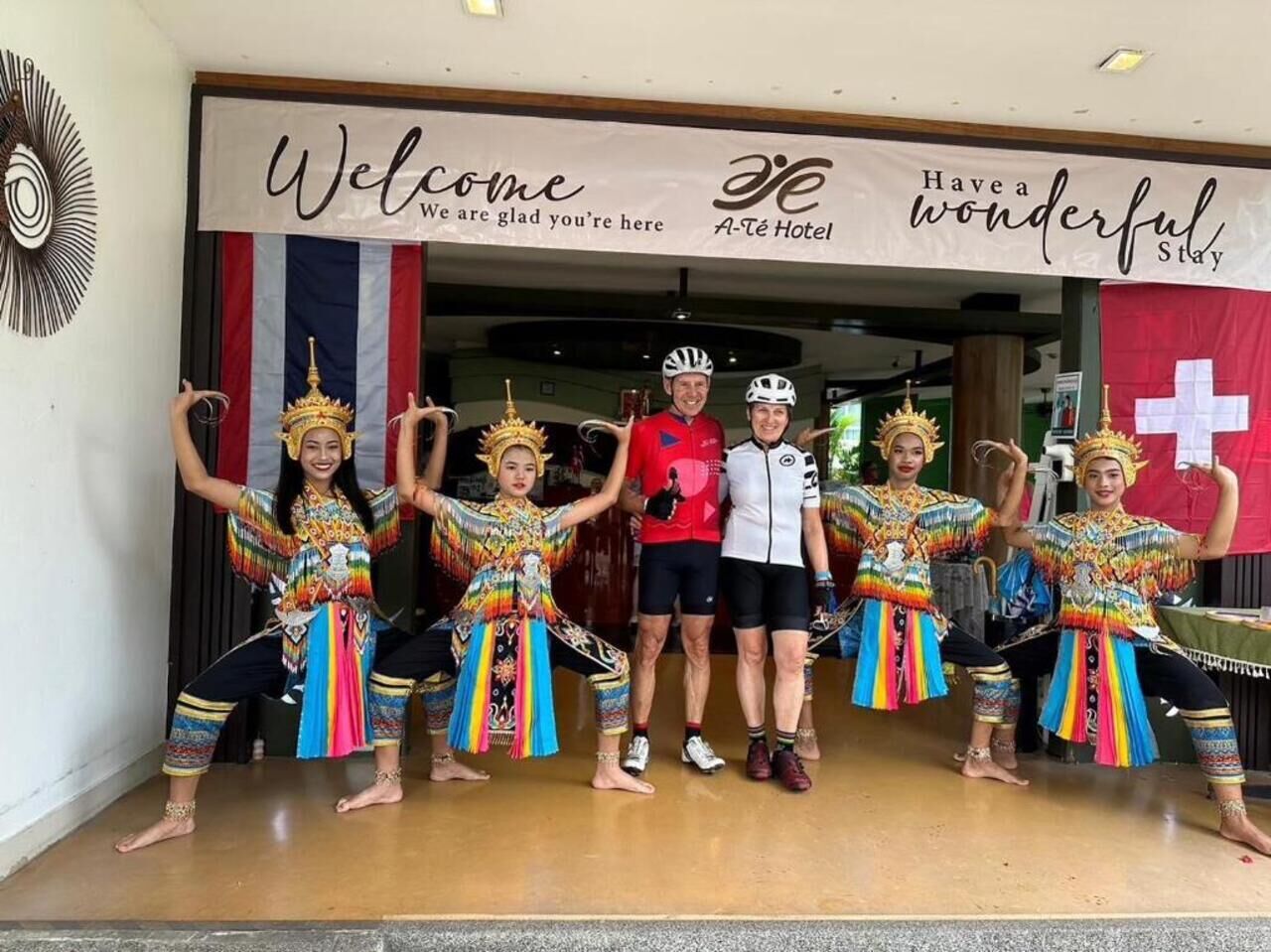 A group of people in colorful traditional attire posing in front of a hotel entrance with a welcome banner.