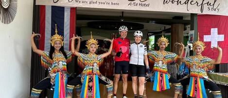 A group of people in colorful traditional attire posing in front of a hotel entrance with a welcome banner.