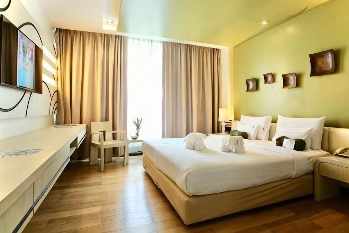 A hotel room with a bed, a desk, a chair, a TV, and a window with curtains.