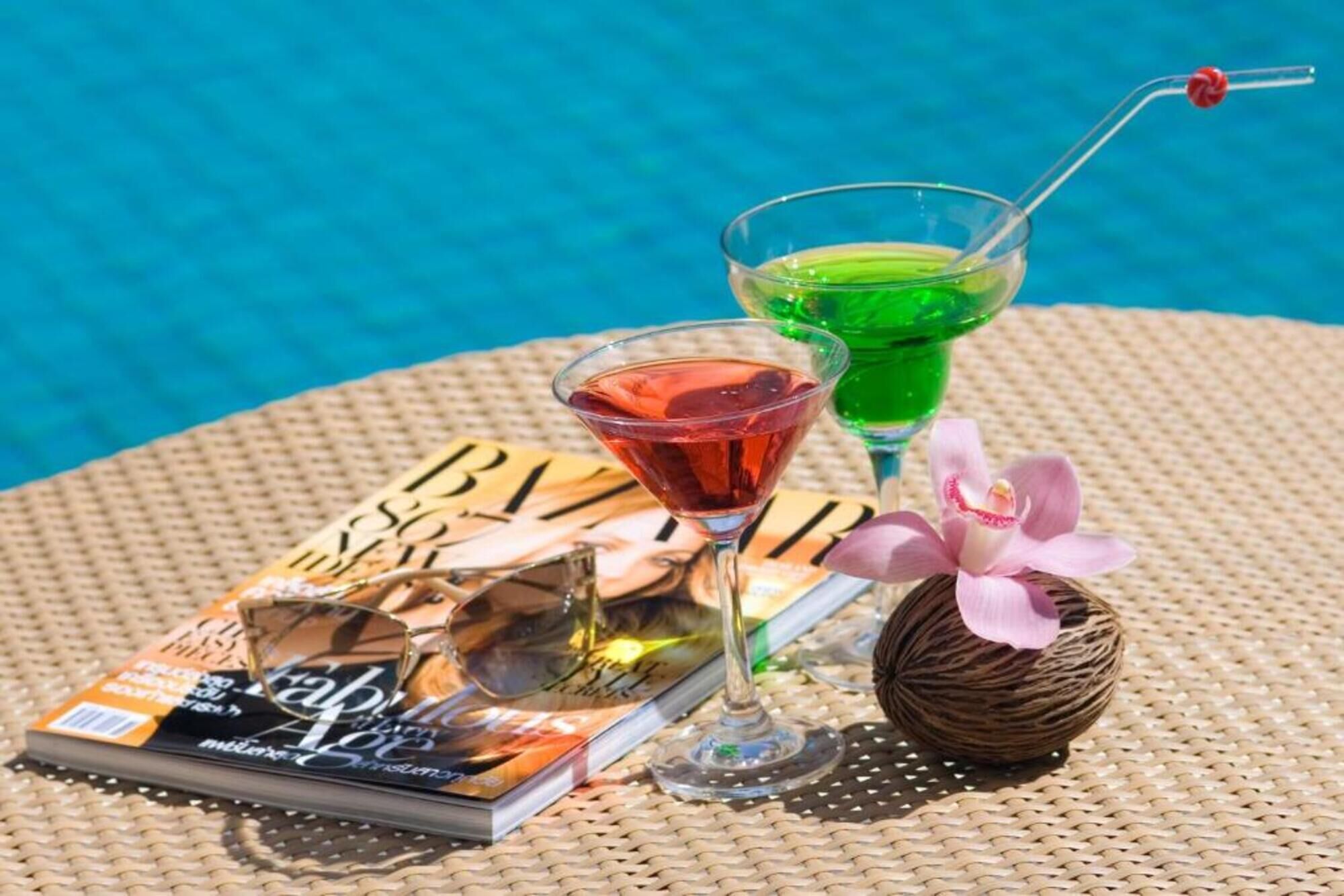 A table with a magazine, two drinks, and a decorative item by a pool.