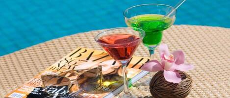 A table with a magazine, two drinks, and a decorative item by a pool.