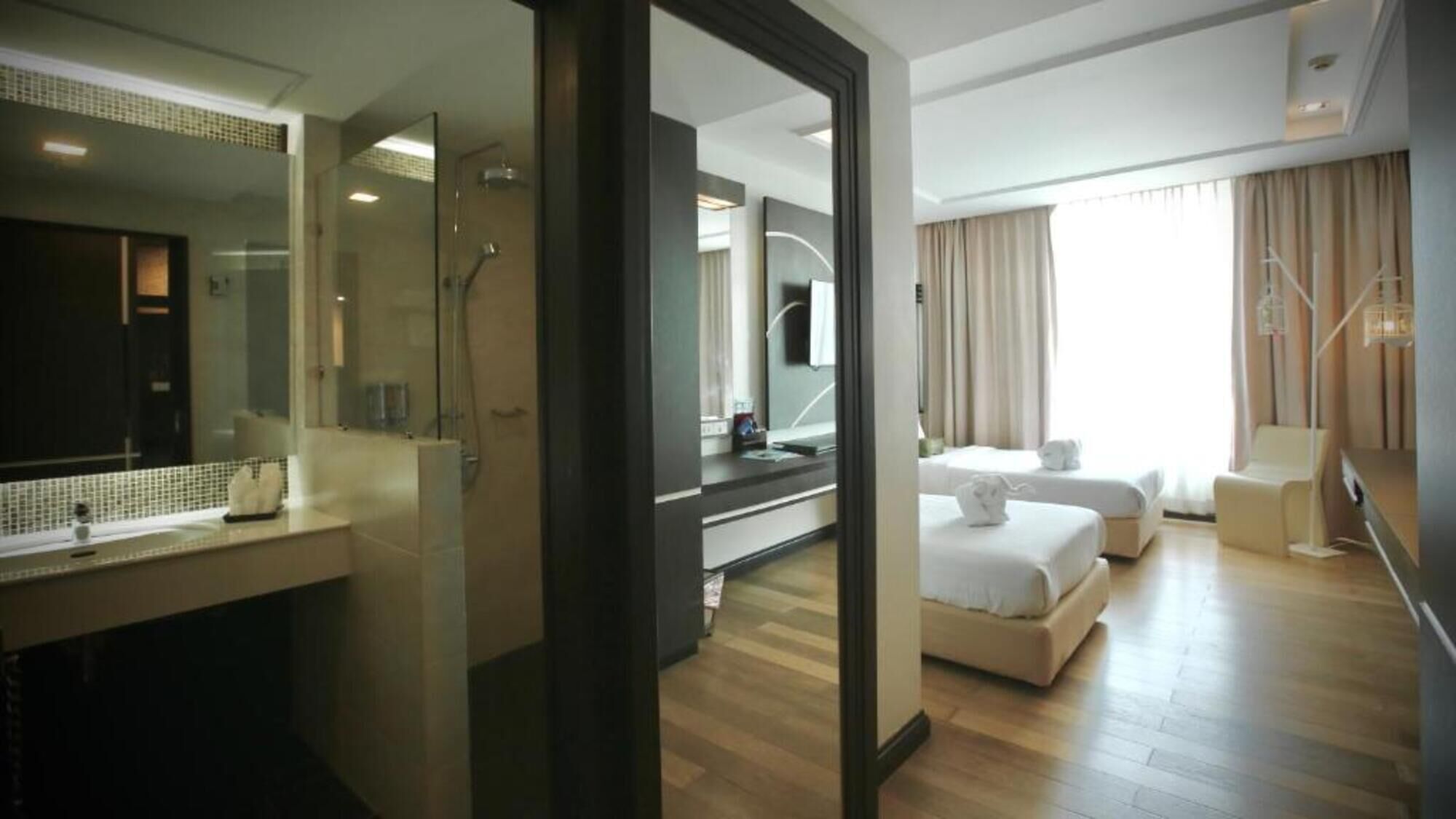 Una habitación de hotel con un espejo grande, ducha, cama, mesita de noche y ventana con cortinas.