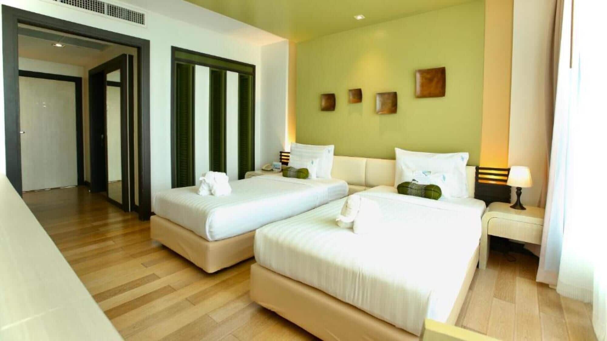 A hotel room with two beds, a wooden floor, and a green wall with artwork.
