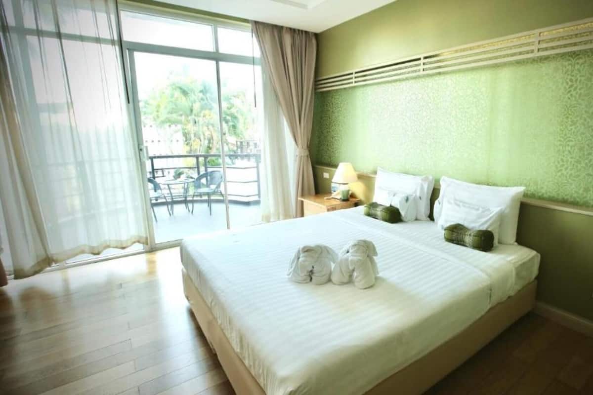 A hotel room with a large bed, a balcony with chairs, and a view of greenery outside.