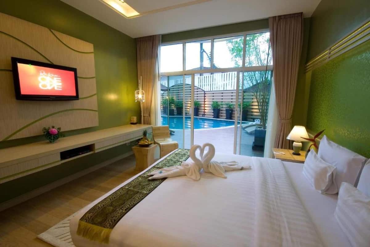 A hotel room with a bed, a TV, a window with a view of a pool, and a nightstand with a lamp.