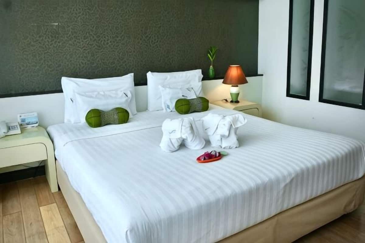 A hotel room with a bed, pillows, a nightstand, a lamp, and a window.