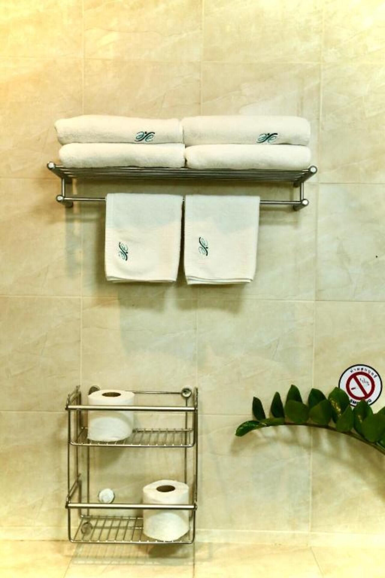 A bathroom with a towel rack holding two towels, a toilet paper holder with rolls, and a no-smoking sign.
