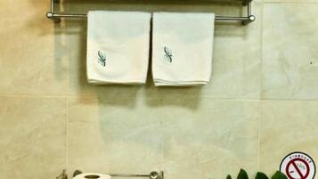 A bathroom with a towel rack holding two towels, a toilet paper holder with rolls, and a no-smoking sign.