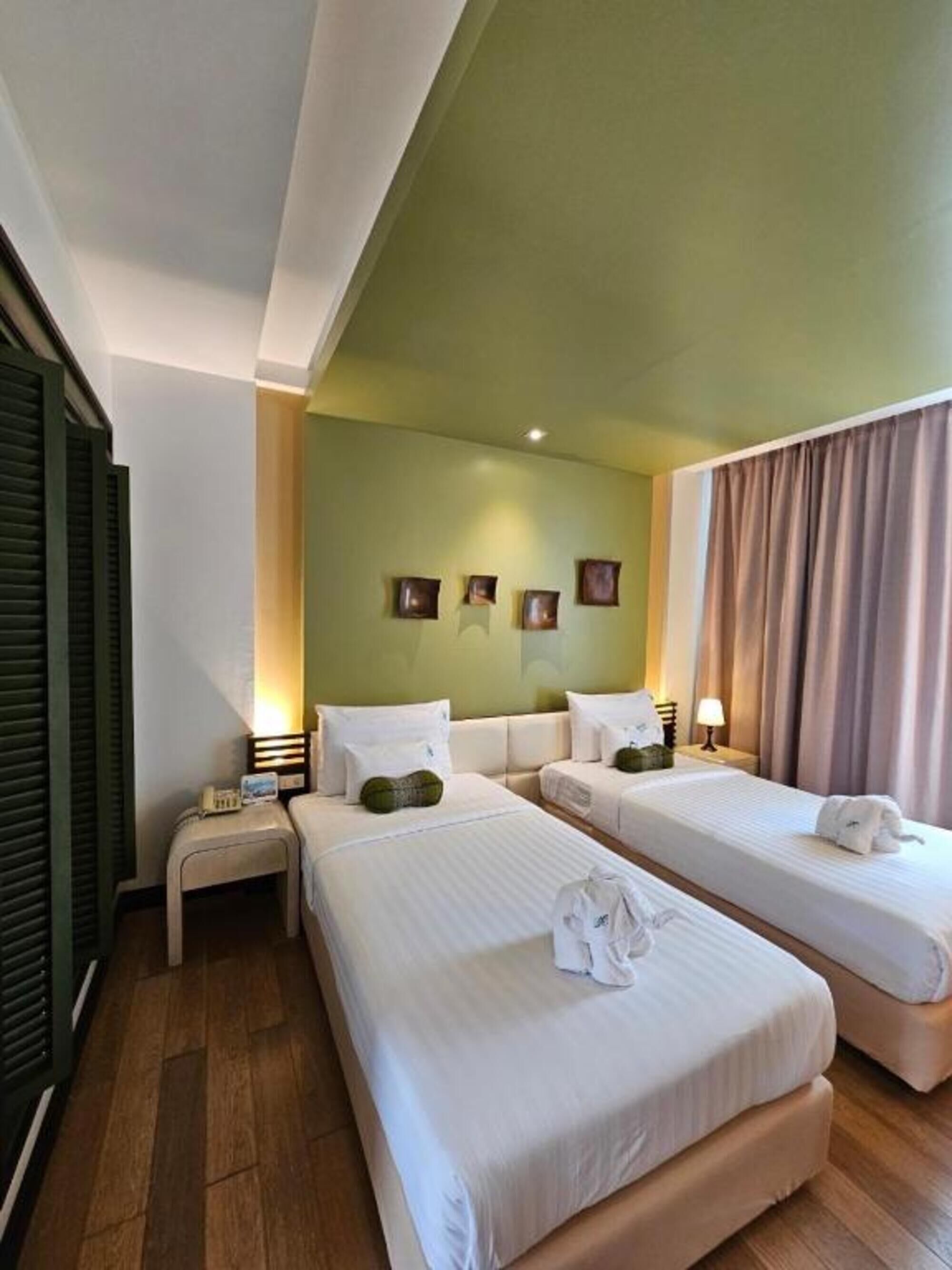 Quarto de hotel com duas camas, uma mesa pequena, um criado-mudo e uma luminária fixada na parede.