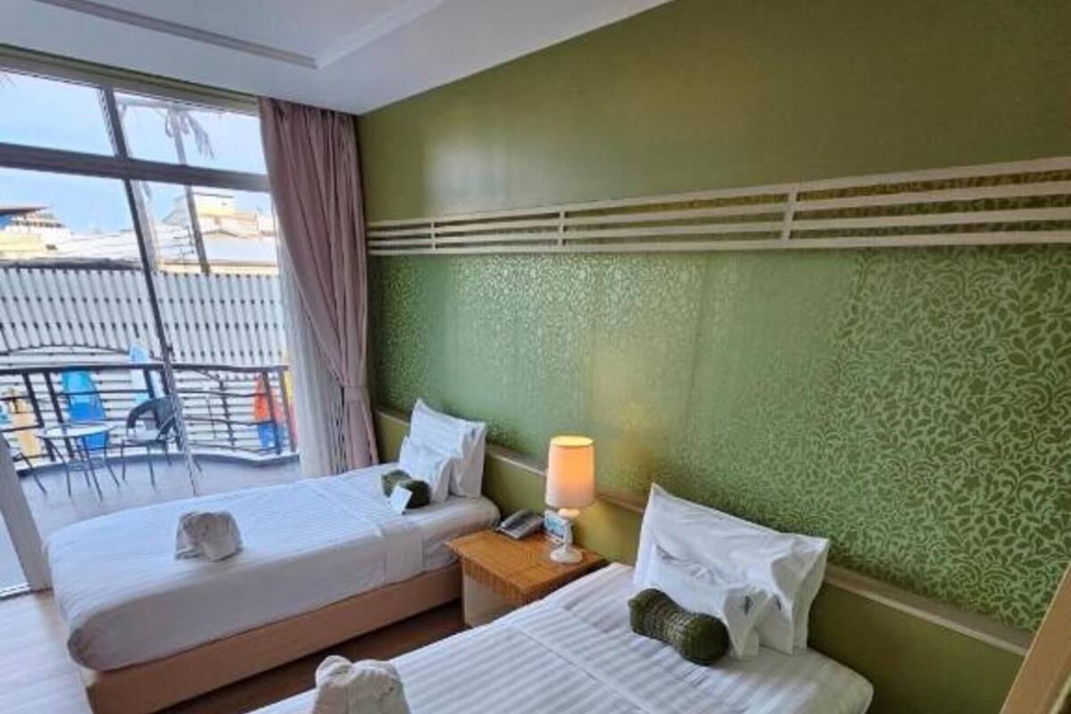 A hotel room with two beds, a nightstand with a lamp, and a view of the outside balcony.
