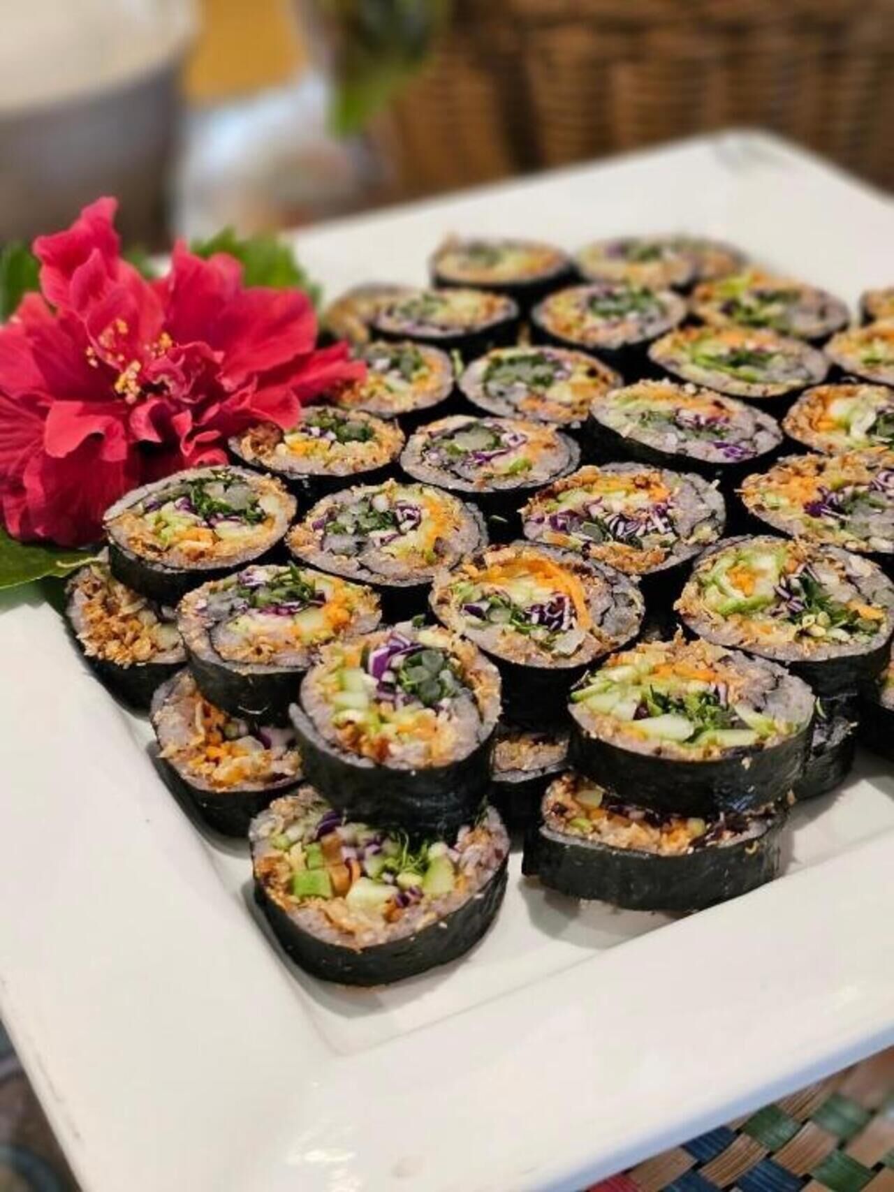 Un plato de sushi con diferentes ingredientes, acompañado de una flor roja.