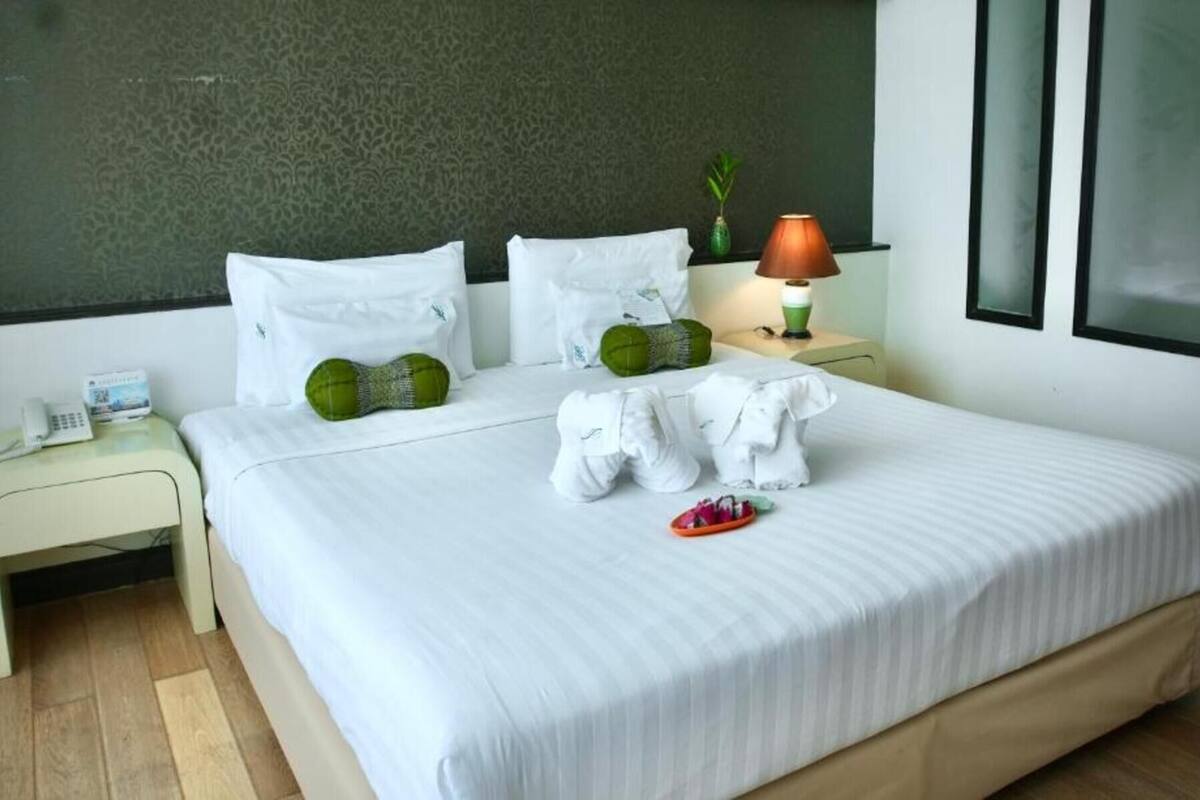 A hotel room with a bed, two pillows, a bedside lamp, a phone, and a small plant.