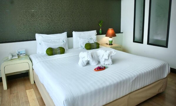Una habitación de hotel con cama, dos almohadas, una lámpara de noche, teléfono y una planta pequeña.