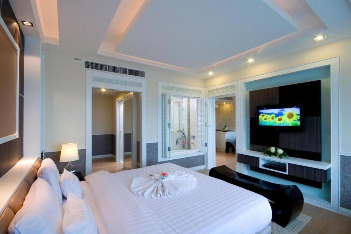 A hotel room with a large bed, a TV on the wall, a bathroom with a shower, and a desk area.