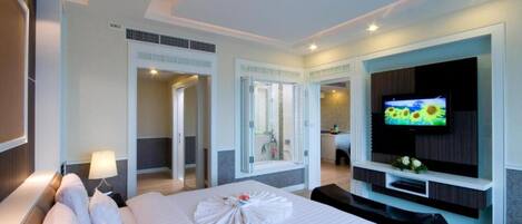 A hotel room with a large bed, a TV on the wall, a bathroom with a shower, and a desk area.