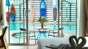 A hotel room with a view of a pool, a dining area, and surfboards on the wall.