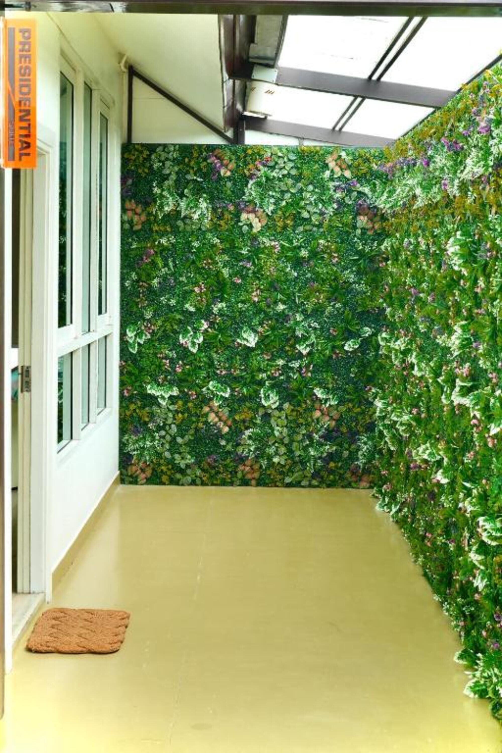 A hallway with a green leafy wall, a yellow floor, and a brown doormat.