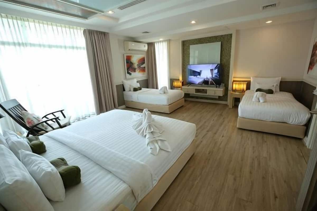 A hotel room with a large bed, a smaller bed, a sofa, a TV, and a desk with a chair.