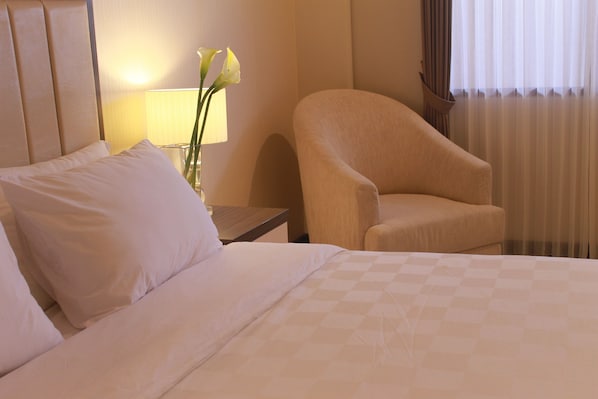 A hotel room with a bed, a chair, a nightstand, a lamp, and a vase with flowers.