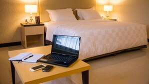A hotel room with a bed, a bedside table with a laptop, a notebook, and a mobile phone. - Bella Hotel Surabaya (Surabaya)