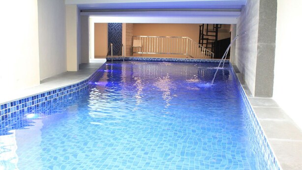 Una piscina interior con agua azul cristalina, bordes de azulejos y una escalera visible que lleva a un nivel superior.