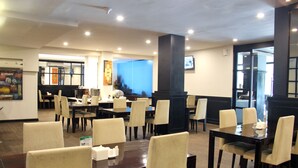 Un restaurante con varias mesas y sillas, un pilar grande y una pantalla de televisión en la pared.