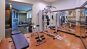 Un gimnasio con equipamiento de ejercicio, una banca y un espejo que refleja el equipo.
