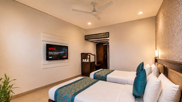 A hotel room with two beds, a TV, a ceiling fan, and a wall-mounted air conditioning unit. - Horizon Hotel (Udaipur)