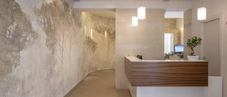 A modern reception area with a wooden reception desk, a large textured wall, and pendant lighting.