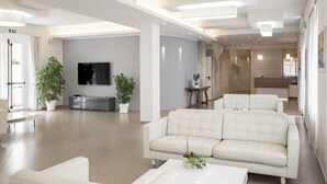 A modern living room with a white sofa, a flat-screen TV, and potted plants. - Hotel La Pineta (Follonica)