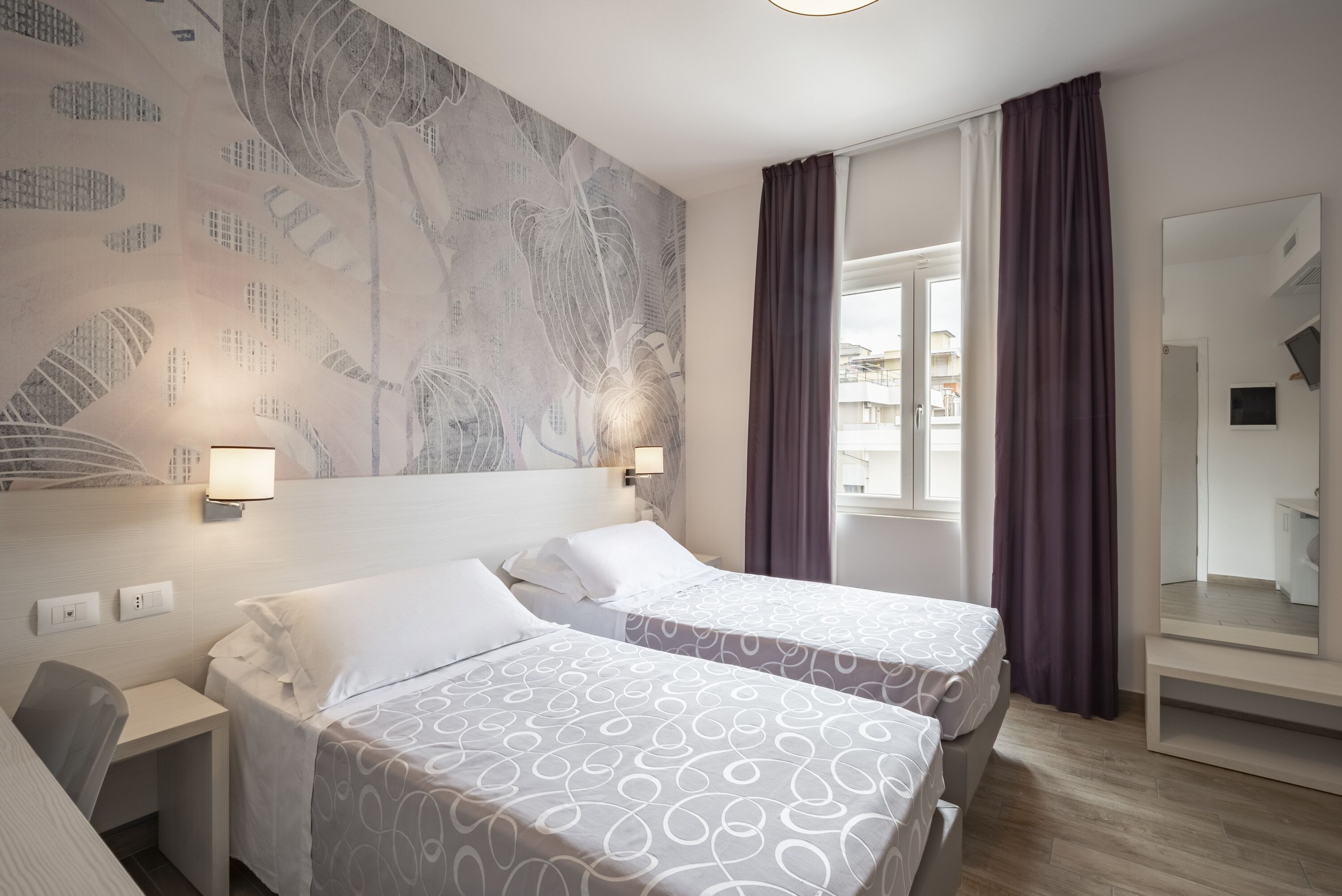 Ein Hotelzimmer mit zwei Betten, einem Schreibtisch, einem großen Spiegel und Blick ins Freie.