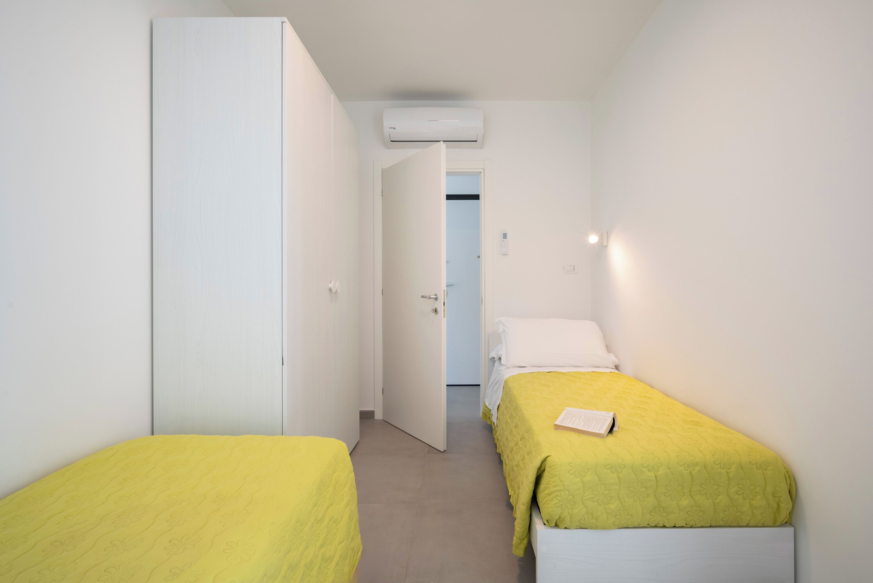 A small, single-room accommodation with two beds, a wardrobe, and a door leading to another room.