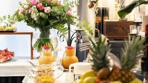 A breakfast table with a variety of fruits, a vase of flowers, and a lamp in the background. - Hotel La Pineta (Follonica)