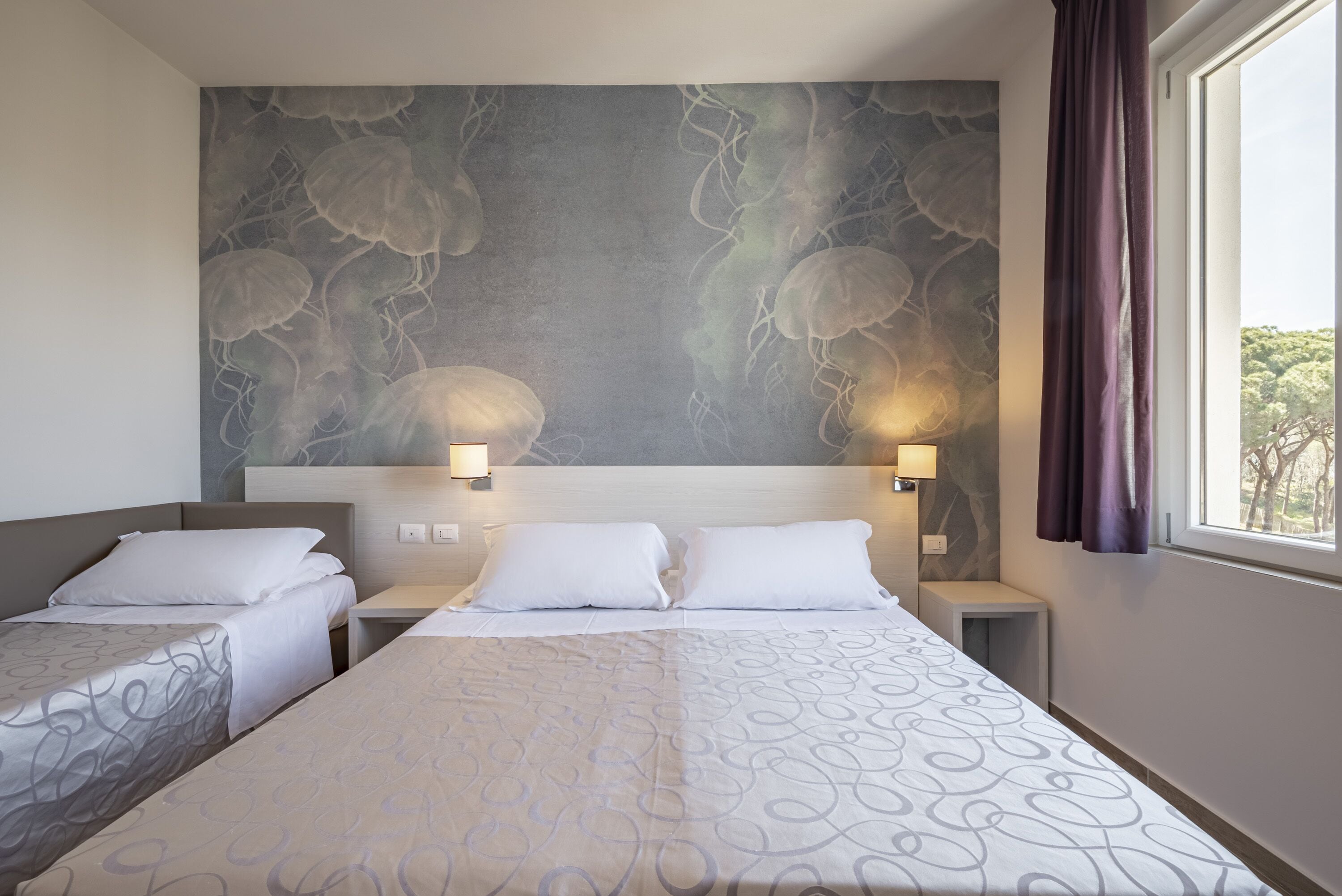 Habitación de hotel con dos camas individuales, un mural grande en la pared y una ventana con cortinas.