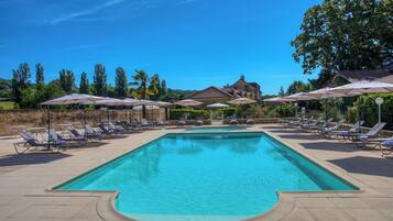 A swimming pool with lounge chairs and umbrellas, surrounded by trees and a building in the background.
