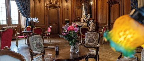 A grand room with ornate wooden paneling, a chandelier, and a round table with chairs.