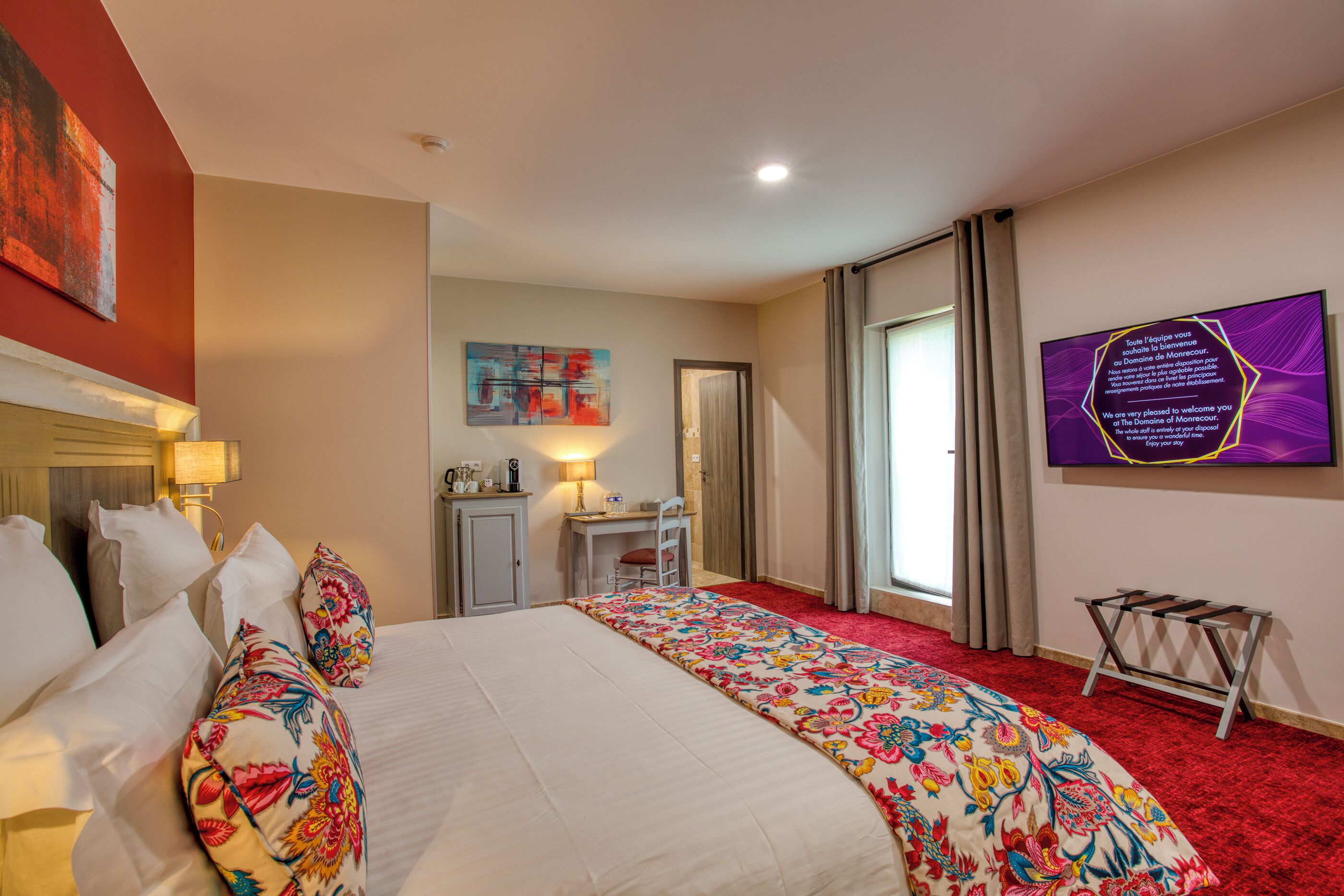 A hotel room with a bed, a desk, a chair, a television, and a window with curtains.