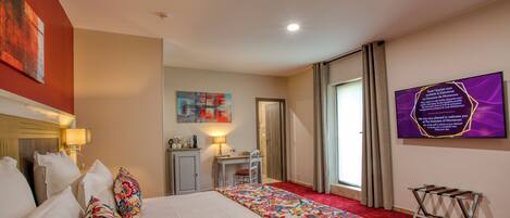 A hotel room with a bed, a desk, a chair, a television, and a window with curtains.