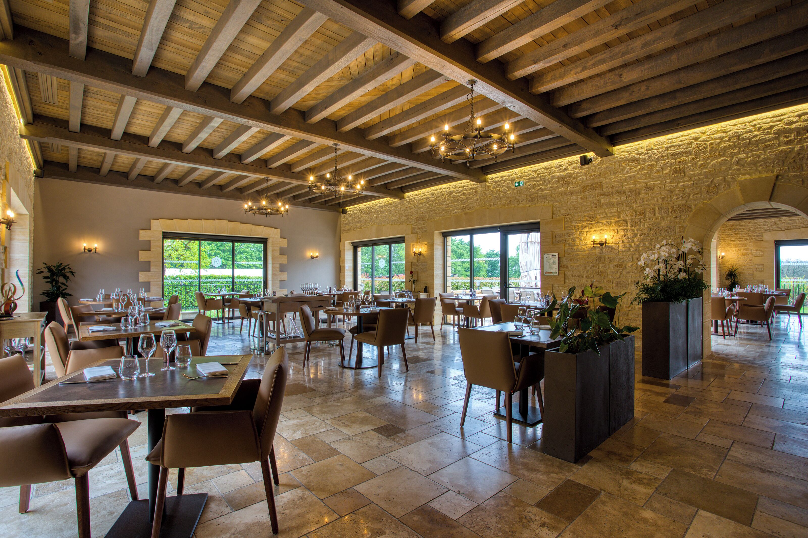 Un restaurante espacioso con techos altos y vigas a la vista, amplias ventanas que ofrecen vistas a zonas verdes, y un interior moderno y pulcro.