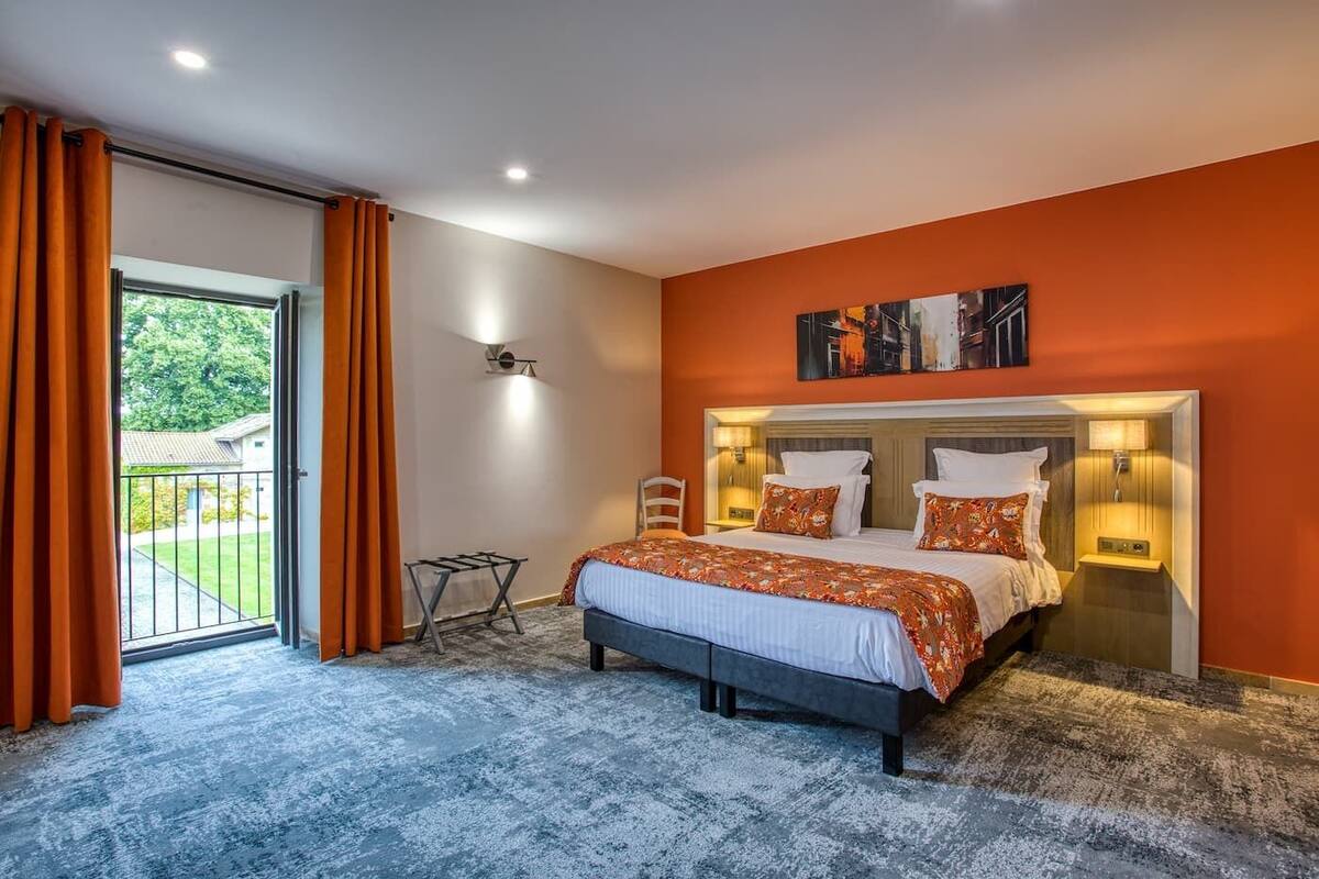 A bedroom with a large bed, two bedside tables with lamps, a view of the outdoors through a sliding door, and a painting on the wall.