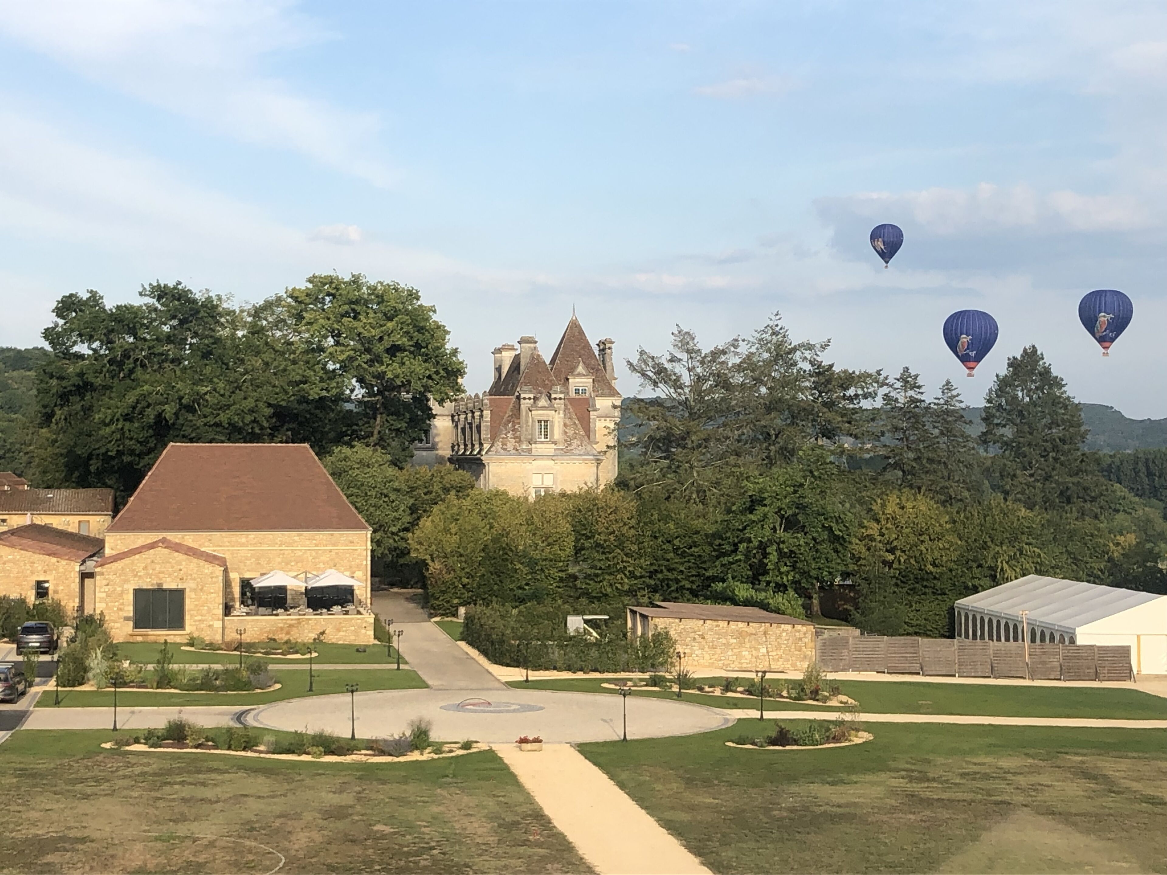 Una extensa propiedad con un césped central, un camino de entrada hacia un edificio y tres globos aerostáticos en el cielo.