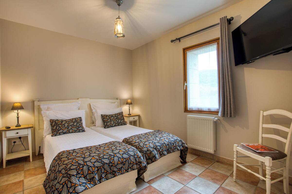 A bedroom with two beds, a TV, a chair, and a window with curtains.