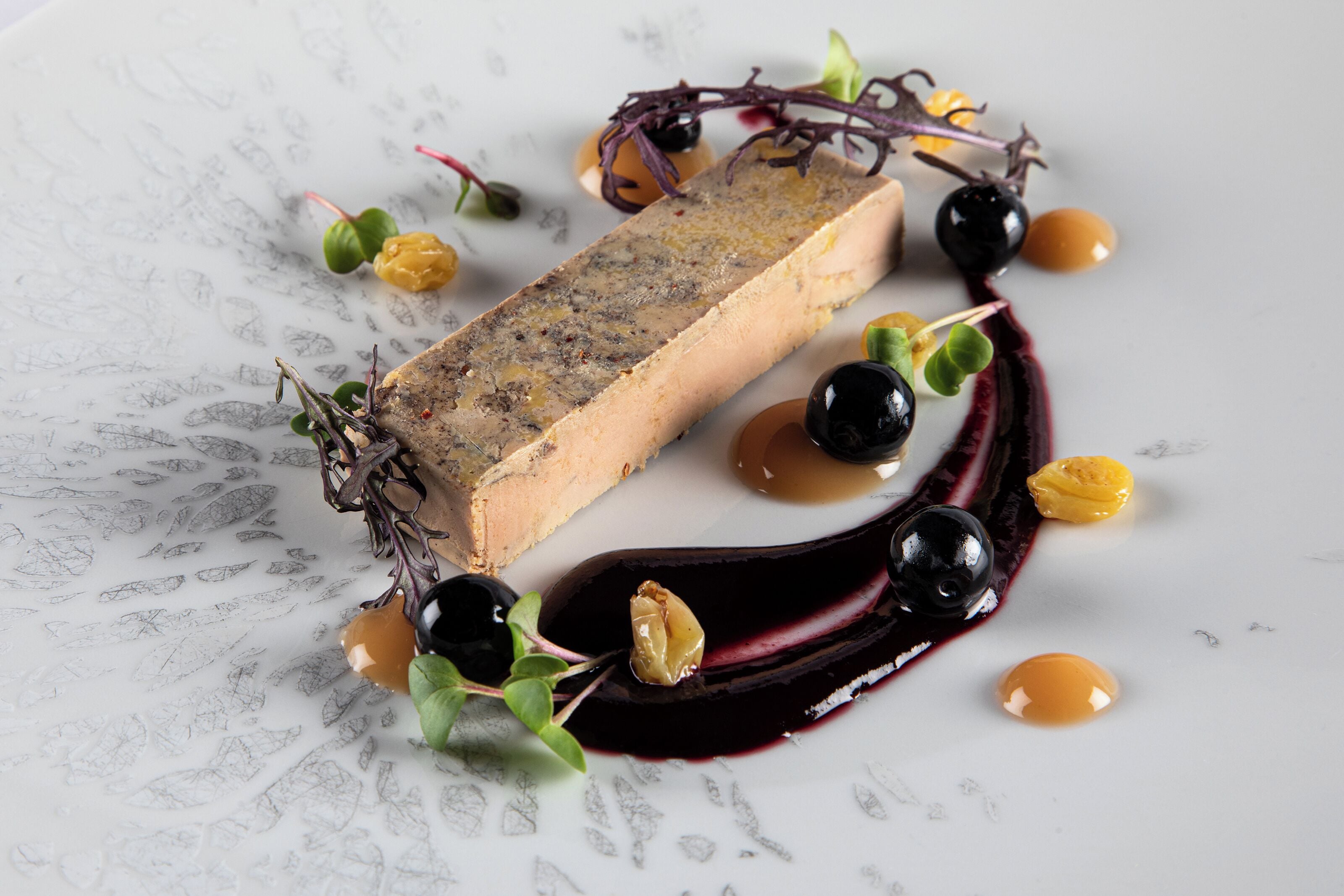 A dish with a rectangular piece of food, possibly terrine, surrounded by various garnishes and sauces on a white plate.