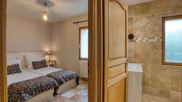 Ein Schlafzimmer mit zwei Betten, einem Nachttisch, einer Lampe und einem Badezimmer mit Dusche und Fenster.