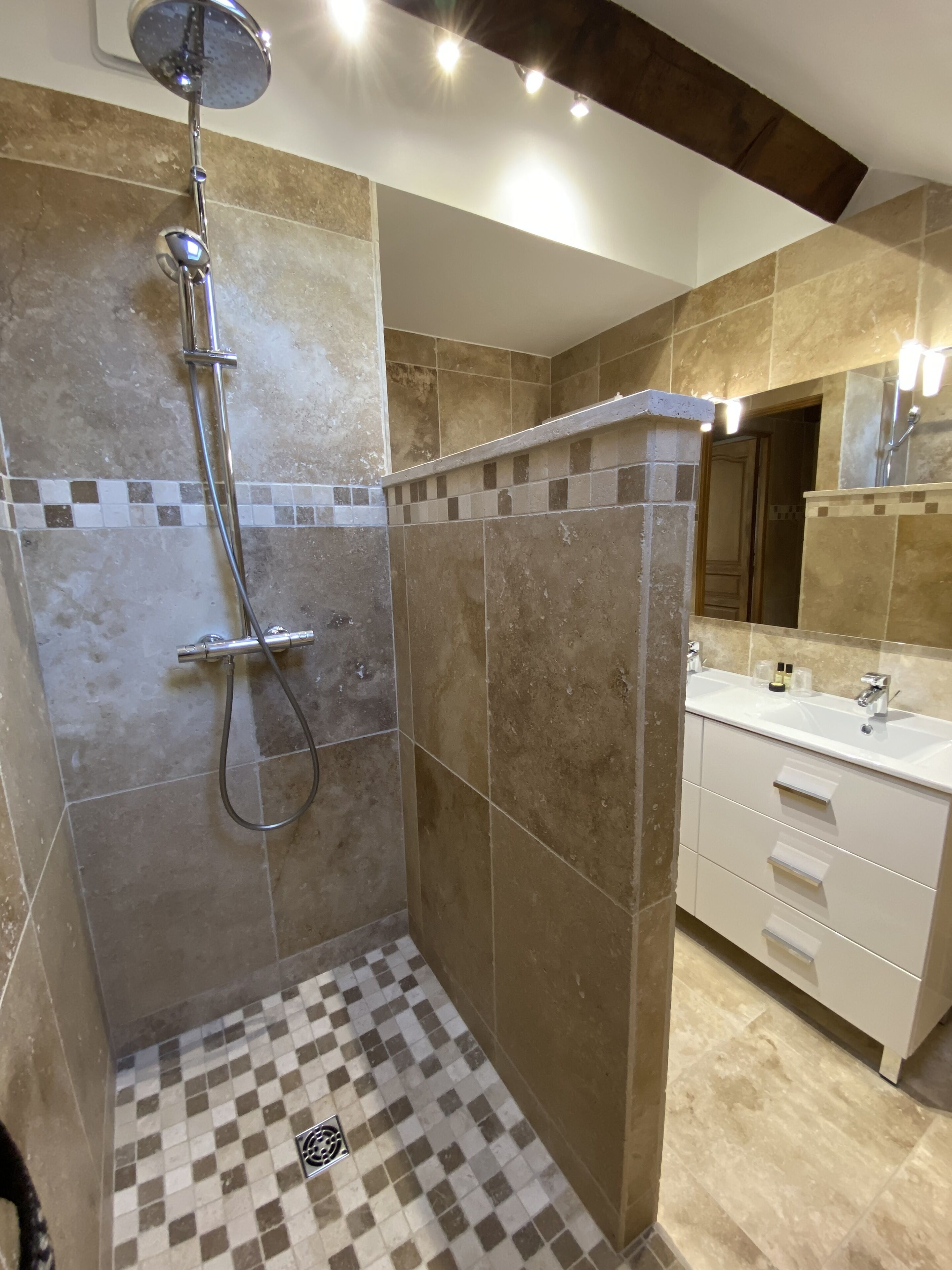 Un baño moderno con ducha, suelo de baldosas y tocador con lavamanos y espejo.