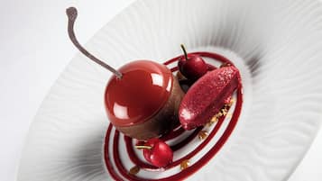 A dessert with cherries and a glossy chocolate sphere on a white plate.