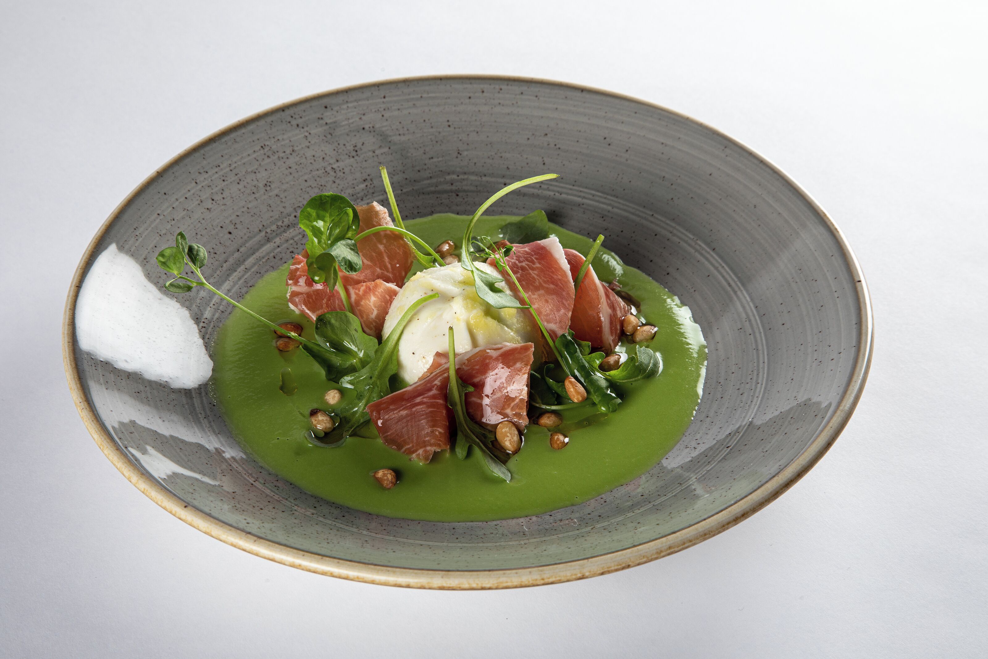 A plate of food with a green sauce, greens, and meat.